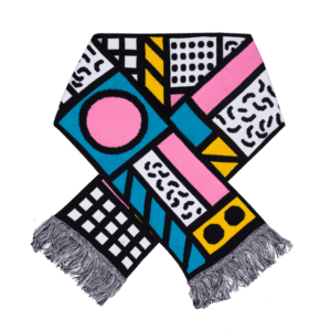 A curated scarf with a bold geometric pattern in black, white, pink, blue, and yellow features various shapes and lines. Finished with grey fringes at the ends, it's laid out in an X shape—a standout find for Tallinn shopping or your favourite concept store. Gate21.ee