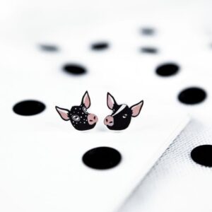 Karud Kõrvarõngad: Two small earrings designed as cartoon pig faces rest on a white surface with black polka dots. These playful earrings highlight curated Estonian design and make a charming gift shop find. Gate21.ee