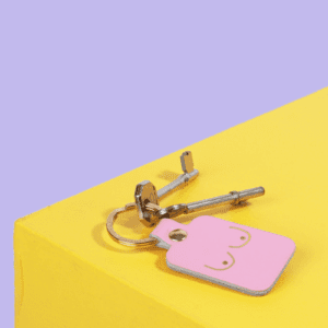 A silver keyring with a pink "Dick Key Ring" rests on the edge of a yellow surface against a purple background, highlighting the playful and bold design often featured in Estonian concept shops. Gate21.ee