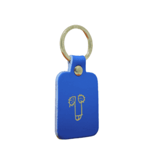 A rectangular red Dick Key Ring with a gold metal split ring, featuring a simple line drawing of a face on the front. Showcasing curated Estonian design against a plain white background. Gate21.ee