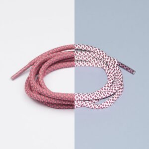 A single Reflective Pink Lace - Extrawize is coiled against a split background; on the left, a white side makes it look pink, whilst on the right, a blue side highlights its white base with red patterns—ideal for concept shops. Gate21.ee