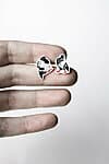 A hand displays Öökullid Kõrvarõngad—small, porcelain earrings with a black-and-white pattern and red adhesive at the crack—against a plain white background, offering unique inspiration for Tallinn shopping enthusiasts. Gate21.ee