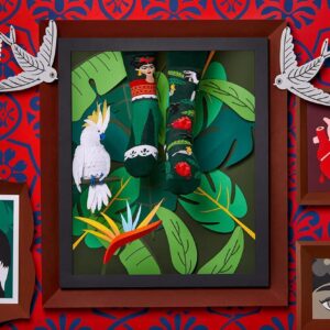 A framed display of green Frida Kahlo socks with floral patterns is accented by tropical leaves and bird decor—a striking shop setup ideal for Tallinn shoppers seeking unique Estonian design. Gate21.ee