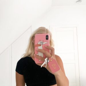 A person with long blonde hair takes a mirror selfie in a white room, holding a pink Dick Keyring alongside their phone. Wearing a short black top, their face is partially obscured as they show off the quirky accessory. Gate21.ee