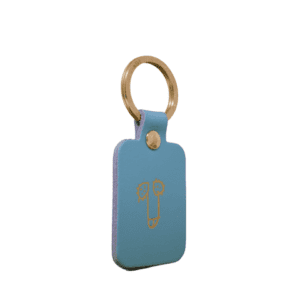 A rectangular red leather Dick Key Ring with a gold metal ring features an abstract gold line drawing of a face—showcasing curated Estonian design and perfect for those seeking unique Tallinn shopping finds. Gate21.ee