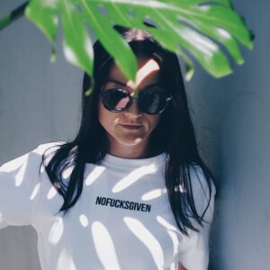 A person stands in partial shade wearing sunglasses and the NOFUCKSGIVEN - Black T-shirt, an effortlessly cool look with a bold statement&mdash;perfect for anyone who loves unique, stylish finds. Gate21.ee