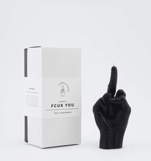 The F*ck You Candle - Black, shaped like a hand with the middle finger raised, stands beside its box, highlighting curated Estonian design and unique handmade craft. Gate21.ee
