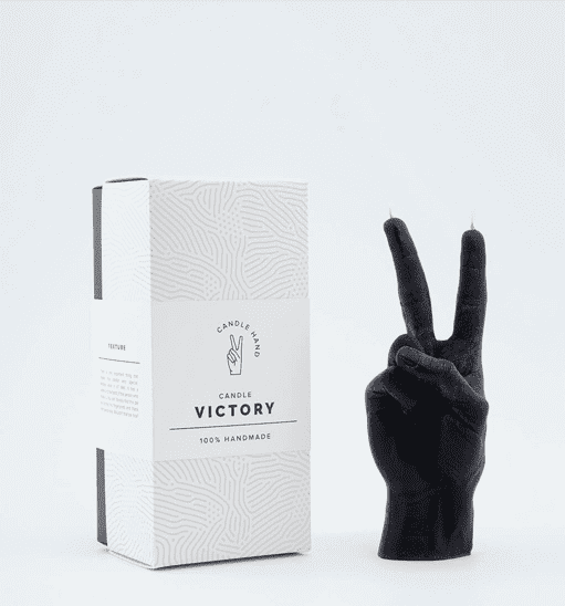 A black candle sculpted in the shape of a hand making a peace sign stands upright next to a white box labelled Victory Candle Hand, 100% Handmade—a curated piece with minimalist style, perfect for any gift shop featuring Estonian design. Gate21.ee
