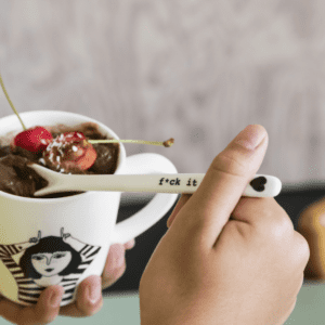 A hand holds the F*ck it Spoon, featuring its bold message on the handle, over a mug of chocolate dessert and cherries&mdash;a quirky choice for anyone searching for unique gifts in a Tallinn concept shop. Gate21.ee