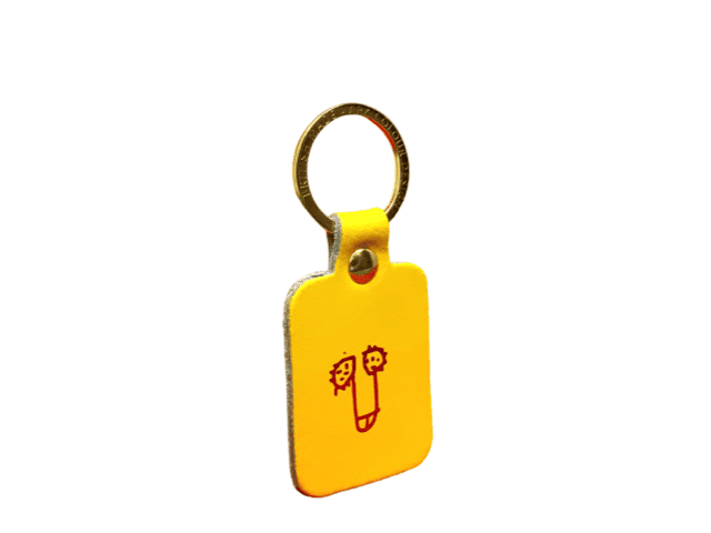 The Dick Key Ring - Red is a yellow rectangular keyring with rounded edges, a metal ring, and a red line drawing of two faces flanking a central vertical shape—perfect for Tallinn shopping. Gate21.ee