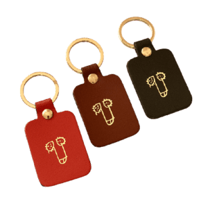 The Dick Key Ring - Red is a rectangular leather keyring with a gold metal ring and a minimalist gold line face design&mdash;ideal for curated finds in Tallinn or as a unique gift shop treasure. Gate21.ee