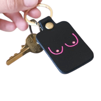 A hand holds the Boob Key Ring - Black, a keyring with two keys. Sold at a Tallinn shopping concept store, it features a minimalist pink outline of two breasts with dot details for nipples. Gate21.ee