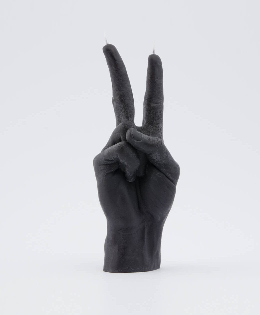 A black candle shaped like a human hand forming a peace sign, with two wicks at the fingertips—this unique idea makes a striking addition to any curated gift shop, set against a plain white background. Gate21.ee
