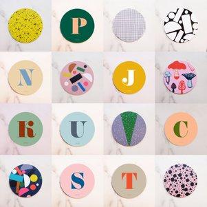 The Hippstory Coasters - KÕIK set includes 16 round coasters featuring Estonian design—some with bold letters (P, N, J, K, U, V, C, T), others with unique abstract or colourful patterns on vibrant backgrounds. Gate21.ee