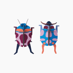 Coccinelle Couple features two vibrant beetle models crafted from flat, interlocking pieces. Celebrating Estonian design, each showcases bold geometric patterns in purple, blue, pink, and orange against a white background. Gate21.ee