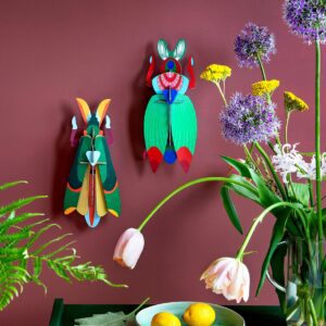 A dark green table topped with the Giant Lobster, curated plates of lemons, a floral vase, and vibrant insect decor on a matte burgundy wall channels the vibe of an Estonian design concept shop. Gate21.ee