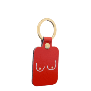 The Boob Key Ring - Red is a rectangular red leather keyring with a gold-coloured ring, featuring a minimalist white line drawing of two breasts—a bold accessory for fans of unique concept shop finds. Gate21.ee