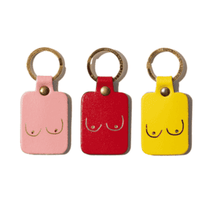 The Boob Key Ring - Red features a rectangular leather keyring in red with a simple gold outline of breasts and a gold metal ring, shown alongside pink and yellow versions on a white background. Gate21.ee