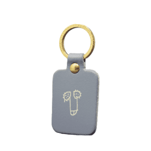 The Dick Key Ring - Grey features a rectangular light grey design with a gold metal ring and two smiling cartoon faces—ideal as a quirky souvenir from Tallinn or a unique find at your favourite concept store. Gate21.ee