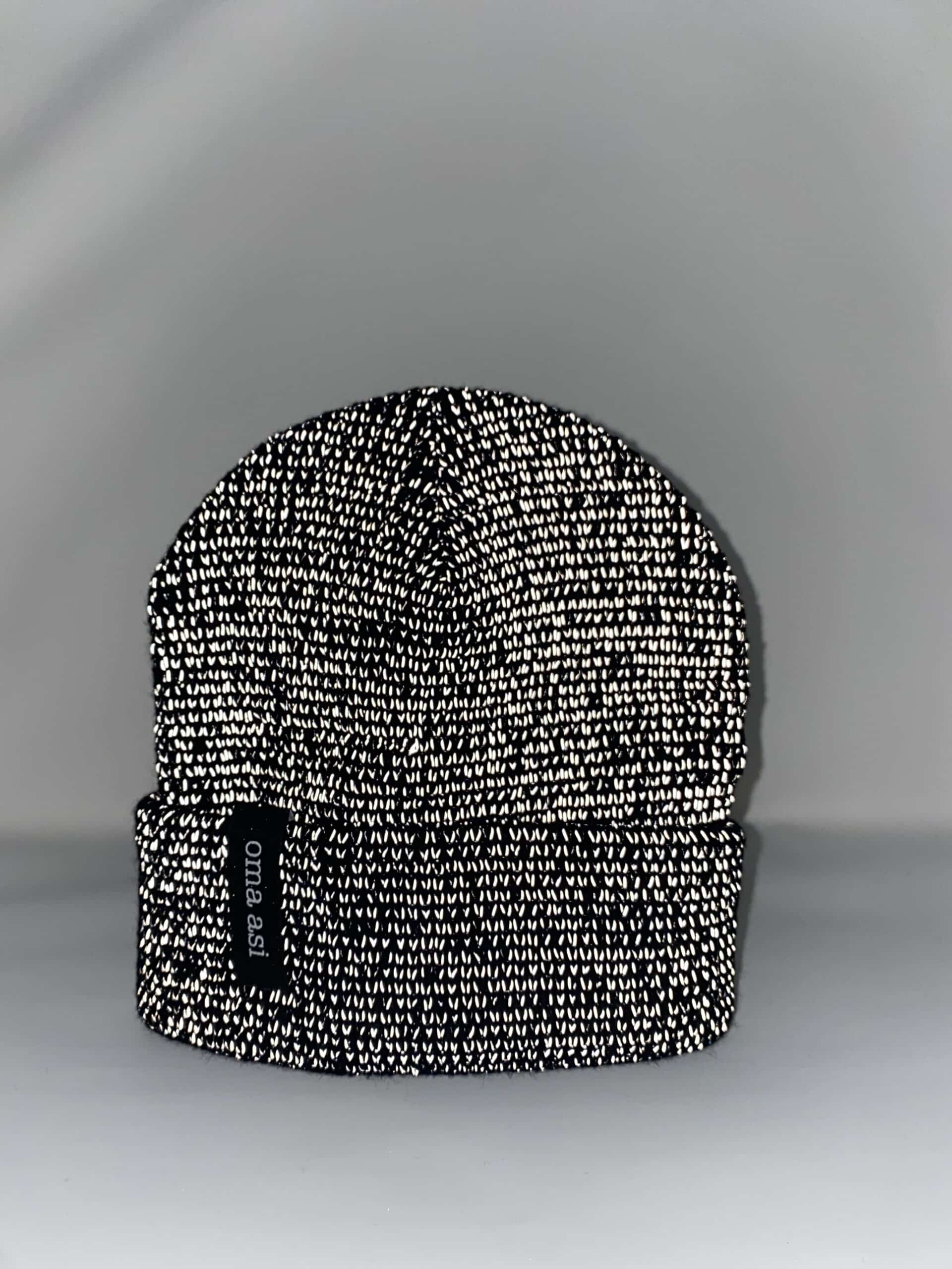 The Reflective Unisex Beanie - Black features a black and white knit with a folded brim, centred on a plain white background. A black tag with "omaaa" celebrates Estonian design—ideal for shopping in Tallinn or as a unique gift. Gate21.ee