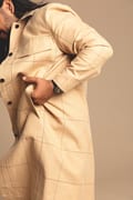 A person adjusts a Black / Gold / 40mm coat with one hand, their face partially out of frame against a beige backdrop—ideal inspiration for Tallinn shopping or exploring fresh finds at a concept shop. Gate21.ee