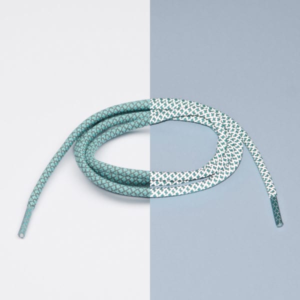 The Reflective Green Laces - Extrawize are coiled on a split surface, their green hues shifting with the background—a standout pick for anyone shopping in Tallinn or browsing local gift shops for unique presents. Gate21.ee