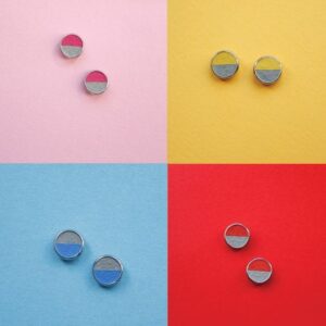 Four pairs of ROUNDS - Concrete - KÕIK stud earrings, inspired by Estonian design, are displayed on pink, yellow, blue, and red backgrounds. Each pair has two-toned halves—one side matching the background and one contrasting for standout style. Gate21.ee