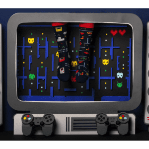 A pair of feet in Game Over video game-themed socks rest on a screen with a retro arcade game, surrounded by controllers and speakers—perfect inspiration for unique ideas at your favourite concept shop. Gate21.ee