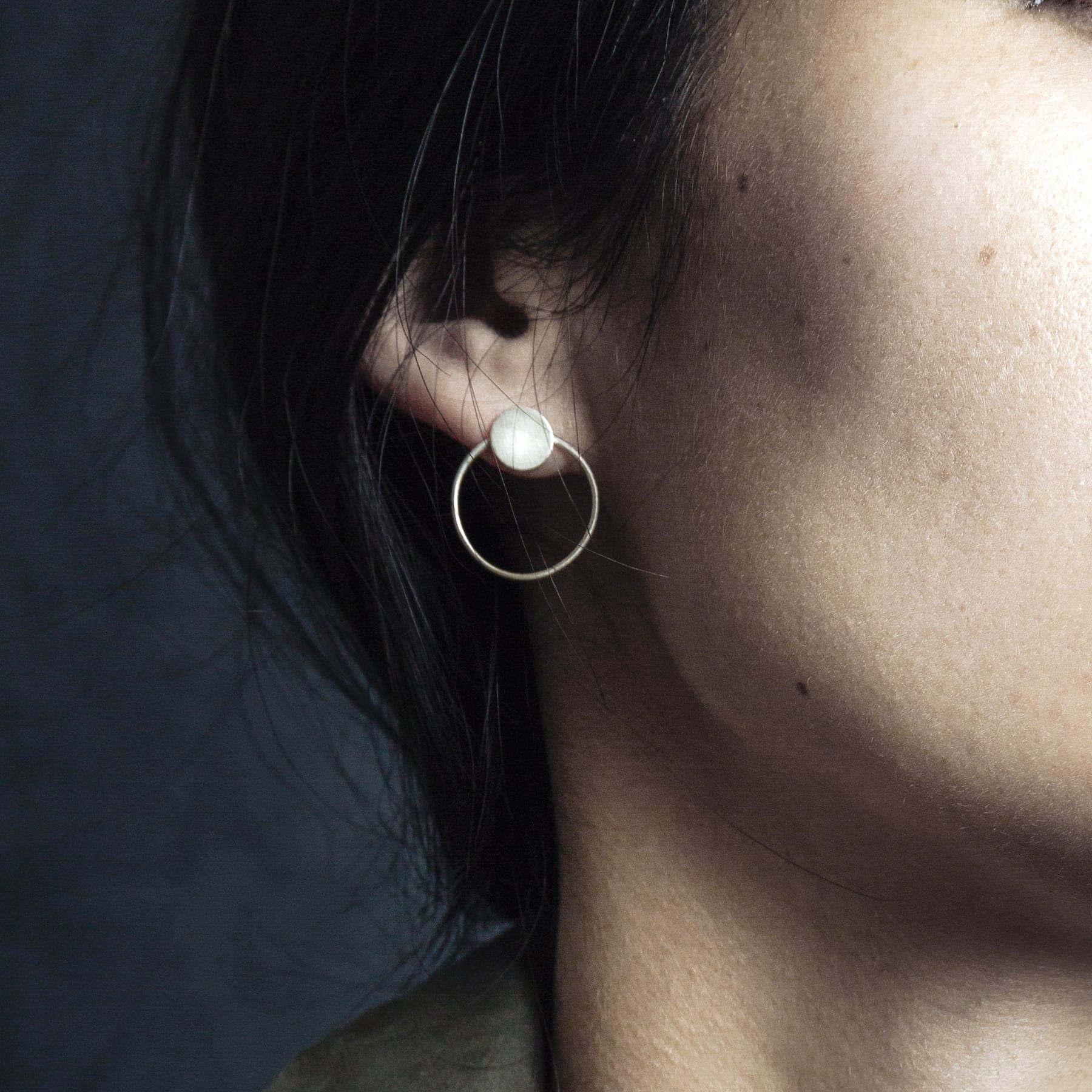 Close-up of a person wearing the Circles on the Water - Silver earring featuring a round silver design with a white sphere at the top, set against a dark background—ideal for fans of unique, concept store-inspired jewellery. Gate21.ee