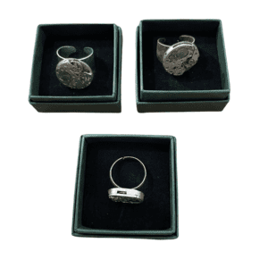 Three Clock rings with intricate watch mechanism designs rest in black velvet boxes, arranged in an upside-down triangle on a white background&mdash;a striking showcase of Estonian design, perfect for any concept shop. Gate21.ee