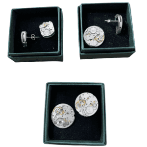 Three green jewellery boxes, each holding a pair of Clock earrings&mdash;round silver pieces with visible watch movement gears and screws inspired by Estonian design&mdash;are displayed on a white background. Gate21.ee