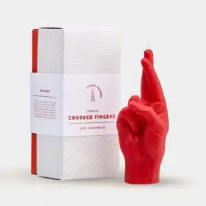 A red Fingers Crossed - Red candle, shaped like a hand with crossed fingers, stands next to its red and white box featuring a subtle fingerprint design. 100% handmade, it's perfect for curated concept shops or gift shops. Gate21.ee