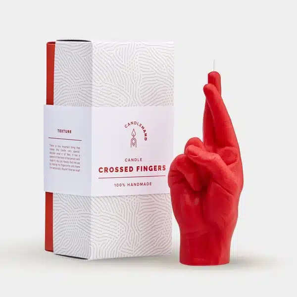A red Fingers Crossed - Red candle, shaped like a hand with crossed fingers, stands next to its red and white box featuring a subtle fingerprint design. 100% handmade, it's perfect for curated concept shops or gift shops. Gate21.ee