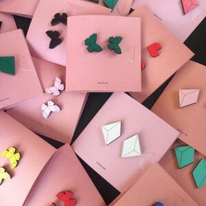 Kirju k&otilde;ik k&otilde;rvar&otilde;ngad earrings in geometric and butterfly shapes, available in various colours, are displayed on overlapping square pink cards&mdash;each card features a unique pair, highlighting Estonian design in the concept store display. Gate21.ee