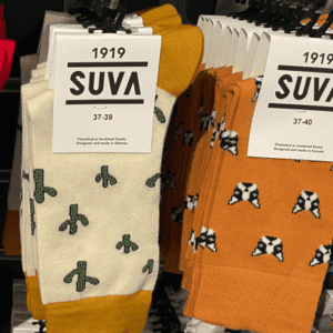 Several pairs of SUVA brand socks, showcasing unique Estonian design, hang on display racks. The white cactus and orange geometric patterns stand out, with sizes 37&ndash;39 and 37&ndash;40 visible on the labels. Gate21.ee