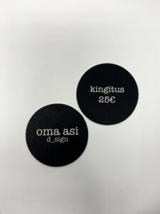 The Oma Asi Gift Card / Kinkekaart features two black circular coasters with unique Estonian design&mdash;one reads "oma asi d_sign," the other "kingitus 25&euro;"&mdash;perfect for Tallinn shopping or as a stylish gift shop find. Gate21.ee