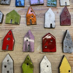 Rectangular ceramic House magnet - &Uuml;llo pieces, each with a door and window, are arranged on wood. Showcasing Estonian design, the glazed magnets feature solid colours and patterns including red, green, purple, and yellow. Gate21.ee
