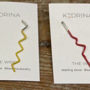 Two KEDRINA cards each display three colourful, zigzag-shaped WIRE EARRINGS: blue, yellow, and silver on the left; red, silver, and black on the right. Both offer unique gift ideas showcased on a wooden surface. Gate21.ee