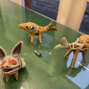 Three small ceramic animal figurines from "Tass nagu + others" by KAURI KALLAS, featuring orange, white, and black patterns, stand on a green surface&mdash;showcasing unique Estonian design from a contemporary concept shop. Gate21.ee