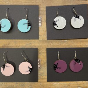 Four pairs of round PIPPIN BIRD earrings feature a bird design and come in teal, white, light pink, and purple. Discover this Estonian design&mdash;ideal for creative ideas or your next Tallinn shopping find. Displayed on a wooden surface. Gate21.ee