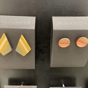 Two pairs of colourful Tass nagu + others - KAURI KALLAS wooden earrings on black displays; one diamond-shaped with layered hues, the other circular with concentric designs. Both are labelled &ldquo;TRIBUVIINEER&rdquo;&mdash;ideal Tallinn gift shop picks. Gate21.ee