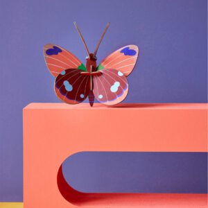 The Delias Butterfly features vivid red, pink, and purple wings perched on a coral structure with a rounded cut-out against a purple background—an eye-catching piece inspired by Estonian design and ideal for unique gift shops. Gate21.ee