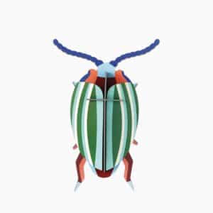 The Rainbow Leaf Beetle is a stylised paper model with green and white stripes, blue antennae, orange legs, and a light blue head&mdash;showcasing curated Estonian design on a plain white background. Gate21.ee