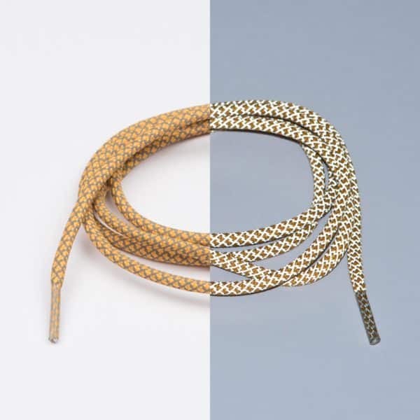 Reflective Rusty Laces - Extrawize are coiled on a vertically split white and grey background, blending tan, gold, black, and white tones in a modern Estonian-inspired style reminiscent of concept shops or gift shops. Gate21.ee