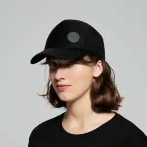 A person with shoulder-length brown hair wears a Double - Black baseball cap and a black T-shirt, posing against a plain grey background—ideal for featuring unique items from an Estonian design gift shop. Gate21.ee