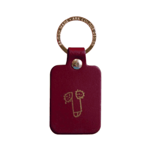 The Dick Key Ring - Oxblood is a rectangular maroon leather keyring with a gold metal ring, featuring a minimalist gold line drawing of a playful face—showcasing curated Estonian design. Gate21.ee