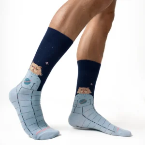 A person wearing Space Cat - Regular socks by Jimmy Lion, which feature a cat in a spacesuit and a grid pattern. The socks showcase dark blue and light blue sections, small spaceship illustrations, and an overall space theme against a white background. Gate21.ee