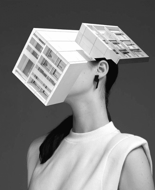 A woman in a sleeveless top with her head replaced by a geometric architectural form evokes the innovative style of Tallinn concept shops. She wears the DUALITY EARRINGS - DOUBLE in this striking black and white image. Gate21.ee