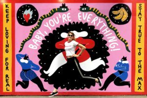 A person poses in front of a colourful mural at a curated concept shop, featuring bold graphics with lips, eyes, stylised figures, and phrases like BABY, YOU'RE EVERYTHING!, KEEP LOVING FOR REAL, and STAY TRUE TO THE MAX—perfect for Tallinn shopping enthusiasts. Gate21.ee