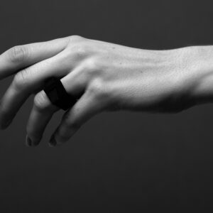 A black-and-white close-up shows an outstretched hand against a dark background, highlighting the DUALITY RING - RIHM on the middle finger—a statement piece reflecting Tallinn’s innovative concept store style. Gate21.ee